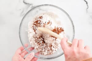 a hand using a wooden spoon to mix dry ingredients