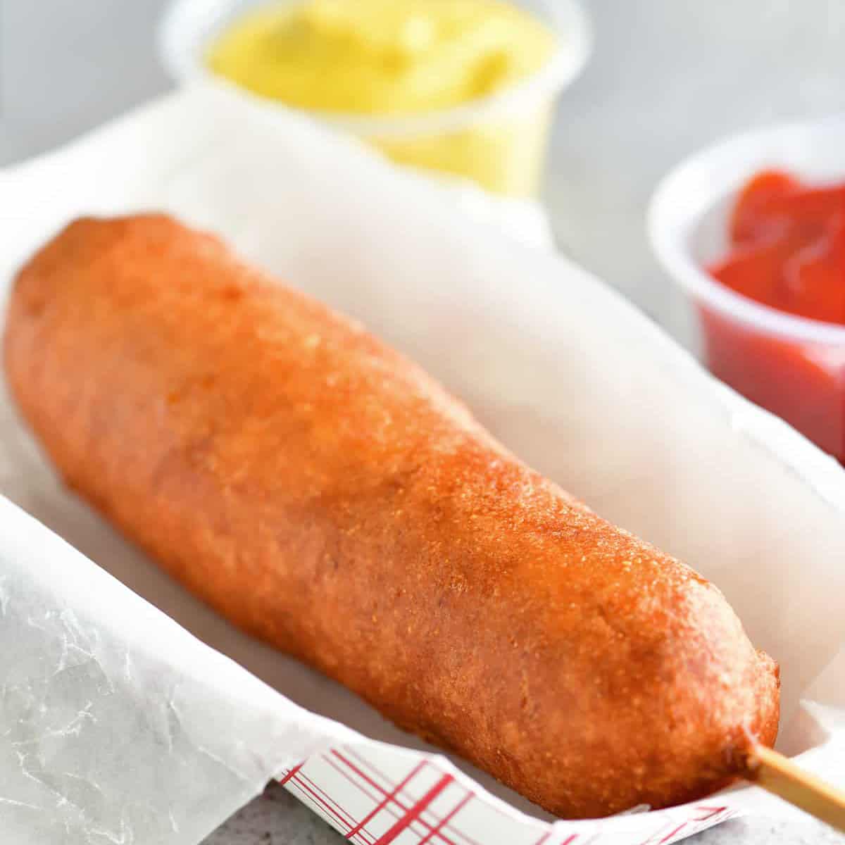honey battered corn dog in a paper tray with condiments