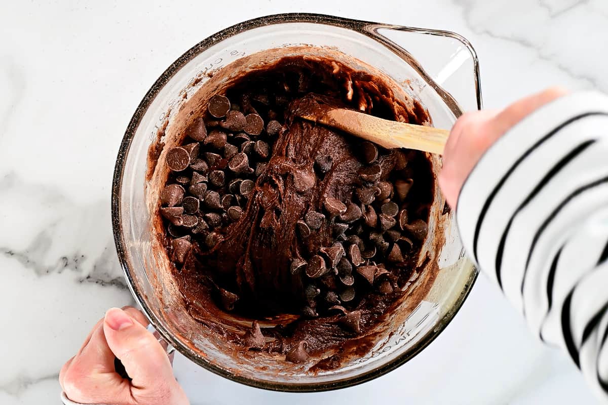hands are shown mixing chocolate chips in to a batter.