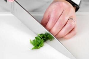 a hand using a chef's knife to chop fresh basil.