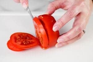 hands using a knife to slice a tomato.