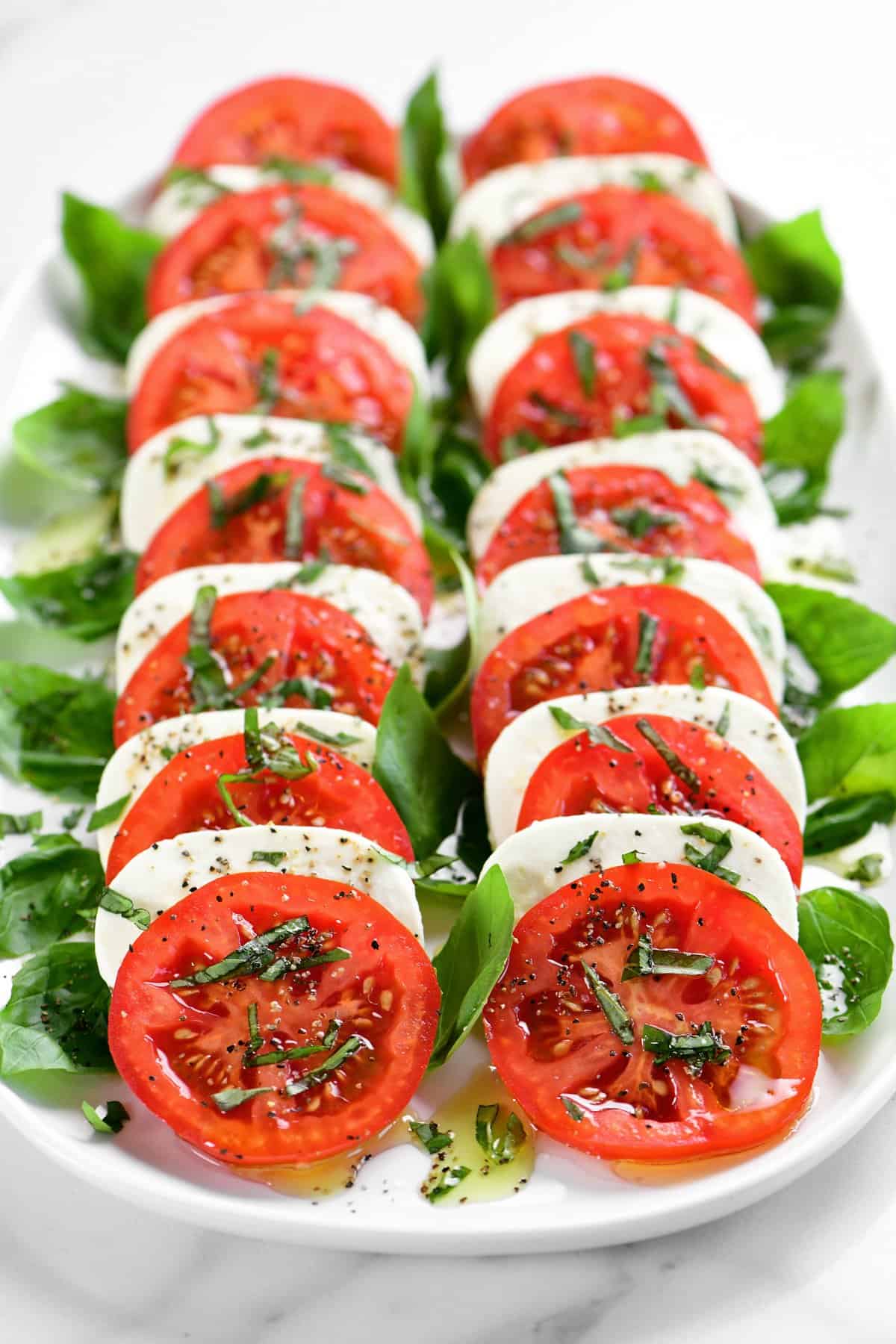 fresh mozzarella cheese and tomatoes, sliced and arranged on a platter with basil leaves and olive oil.