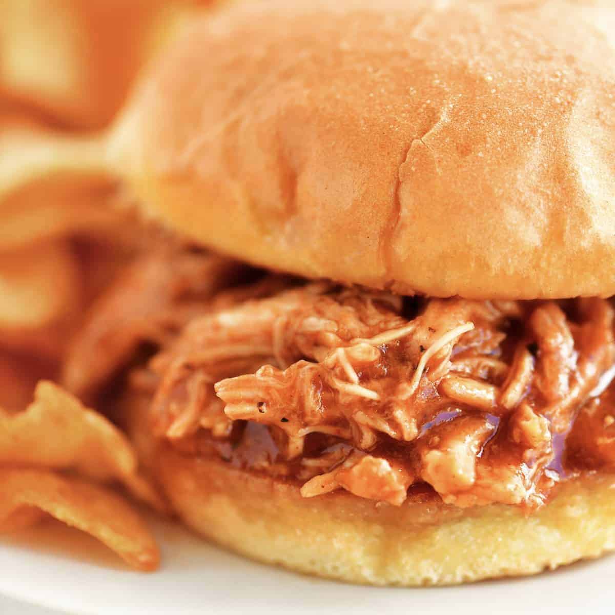 Barbecue chicken sandwich on a plate with chips.