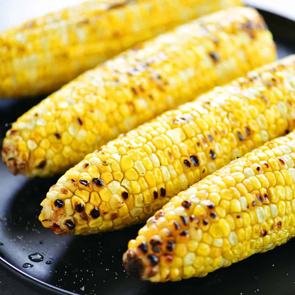 grilled corn on the cob on a black plate.