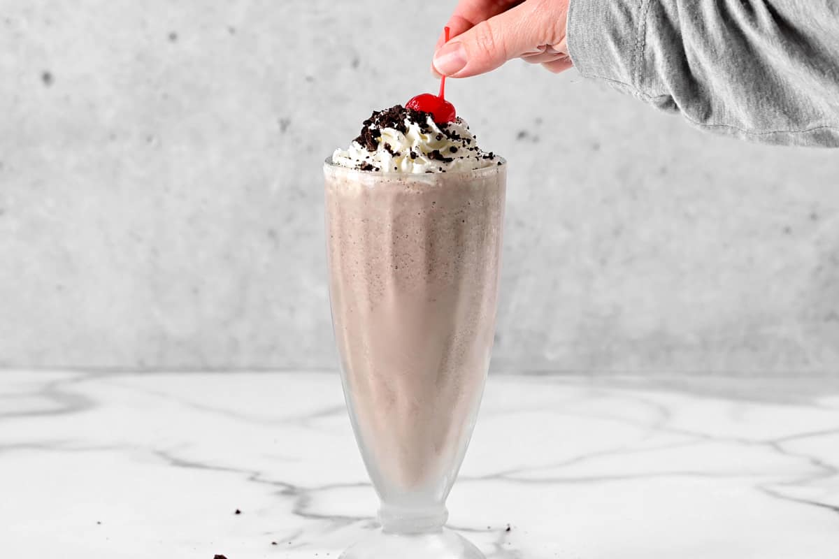 a hand places a cherry on top of a shake.