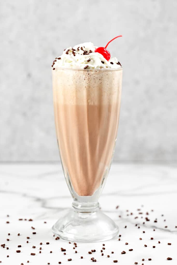 a chocolate milkshake in a milkshake glass with a cherry on top.