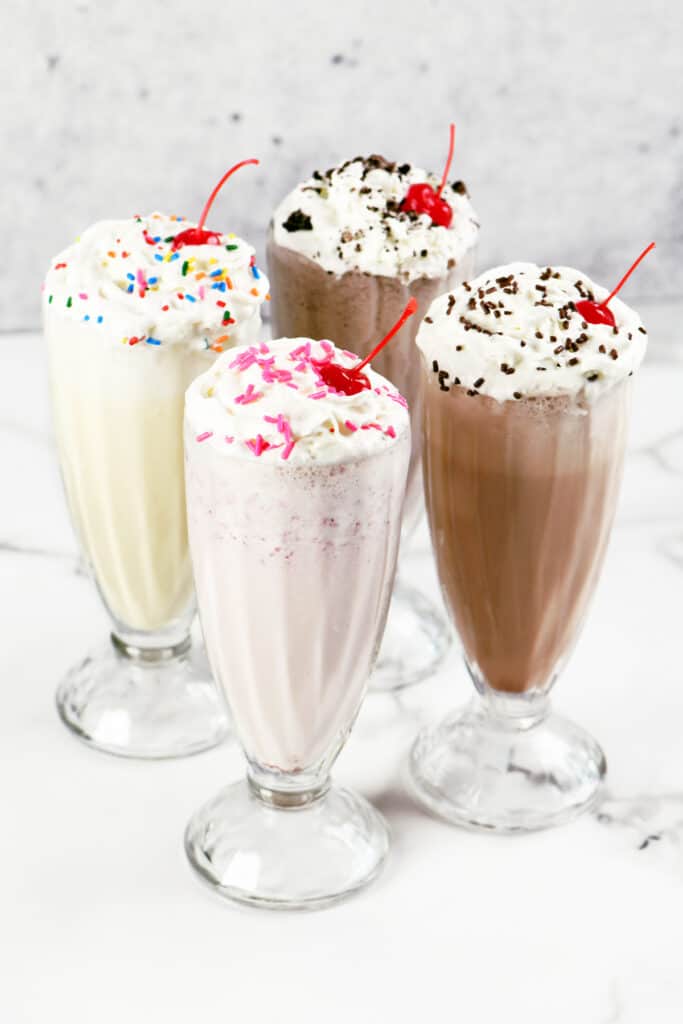 four milkshakes in glasses with whipped cream on top.
