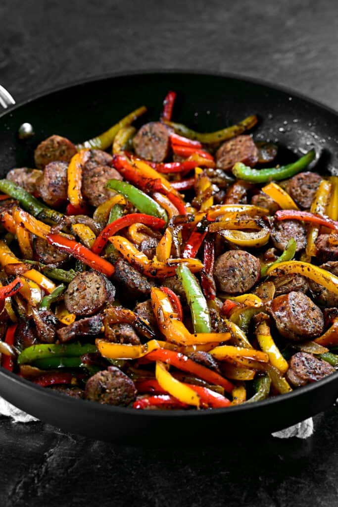 sausage and peppers cooking in a black pan.