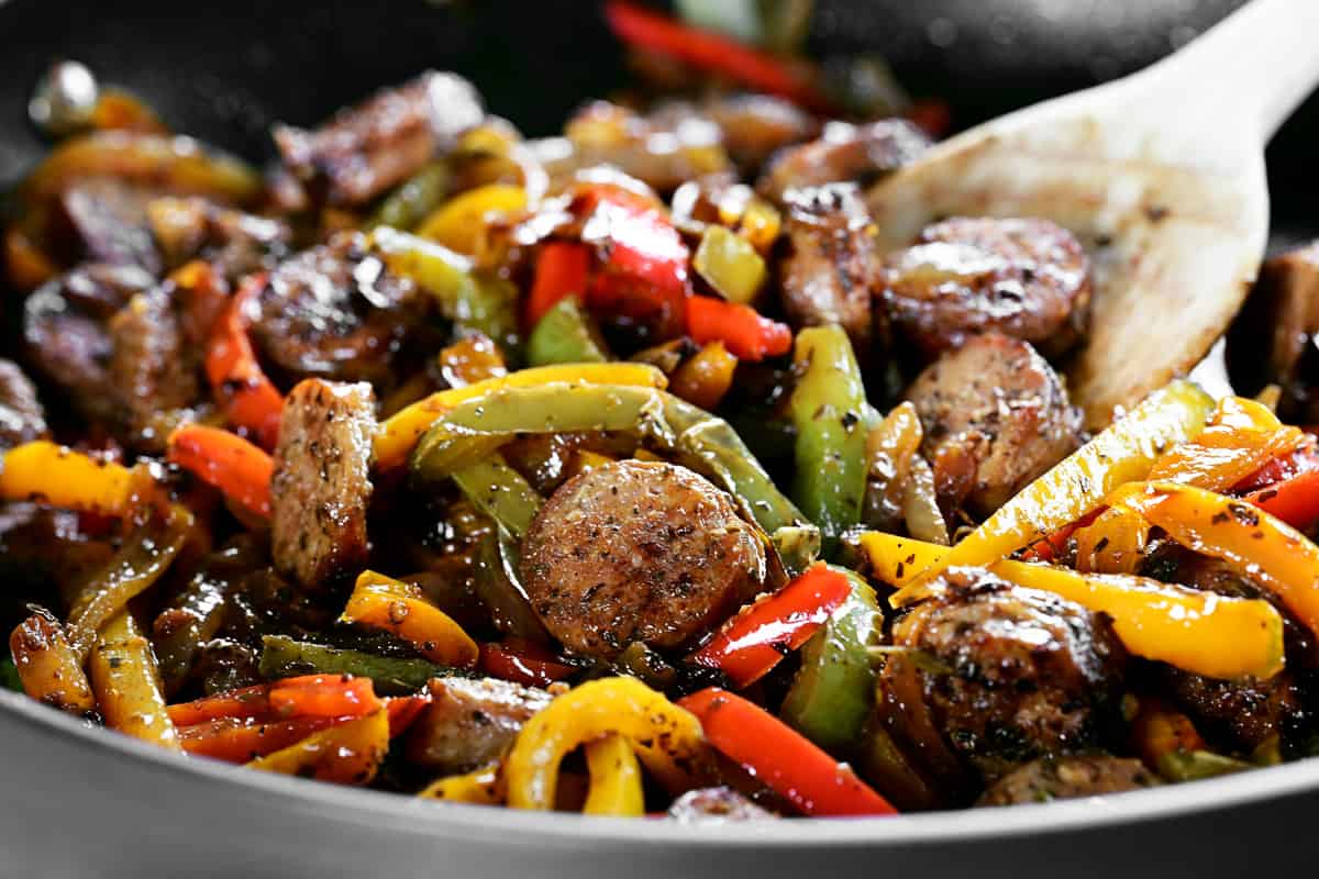 a wooden spoon in a pan with veggies and meat frying.