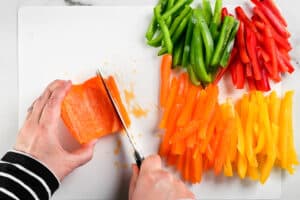 hands using a knife to slice bell peppers.