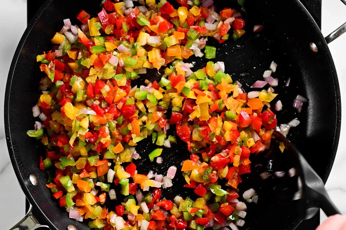 a spatula stirring diced peppers in a frying pan.