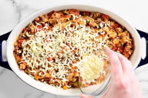 a hand adding shredded cheese to the casserole.