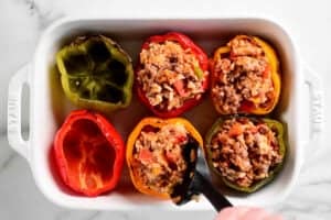 a hand uses a black spoonula to fill the stuffed peppers.