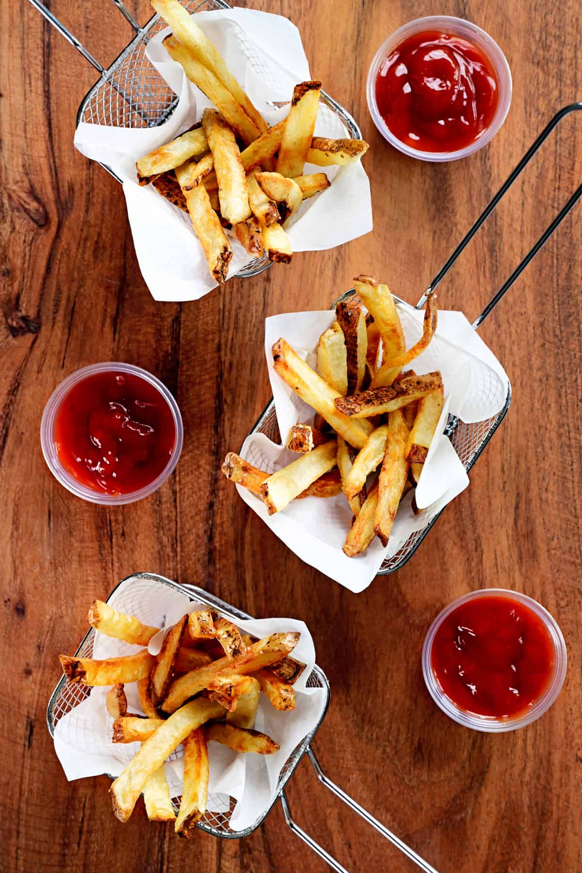 three wire baskets of air fryer french fries and containers of ketchup.