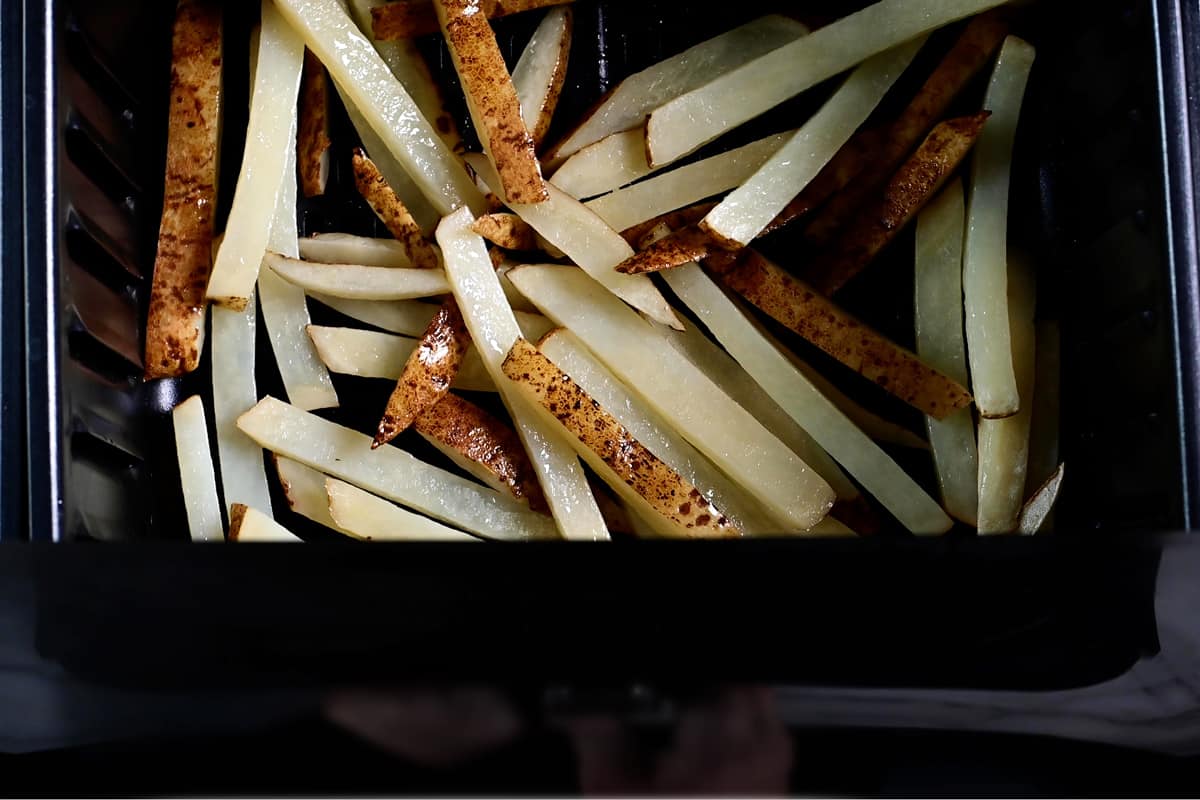 partially baked french fries in an air fryer basket.