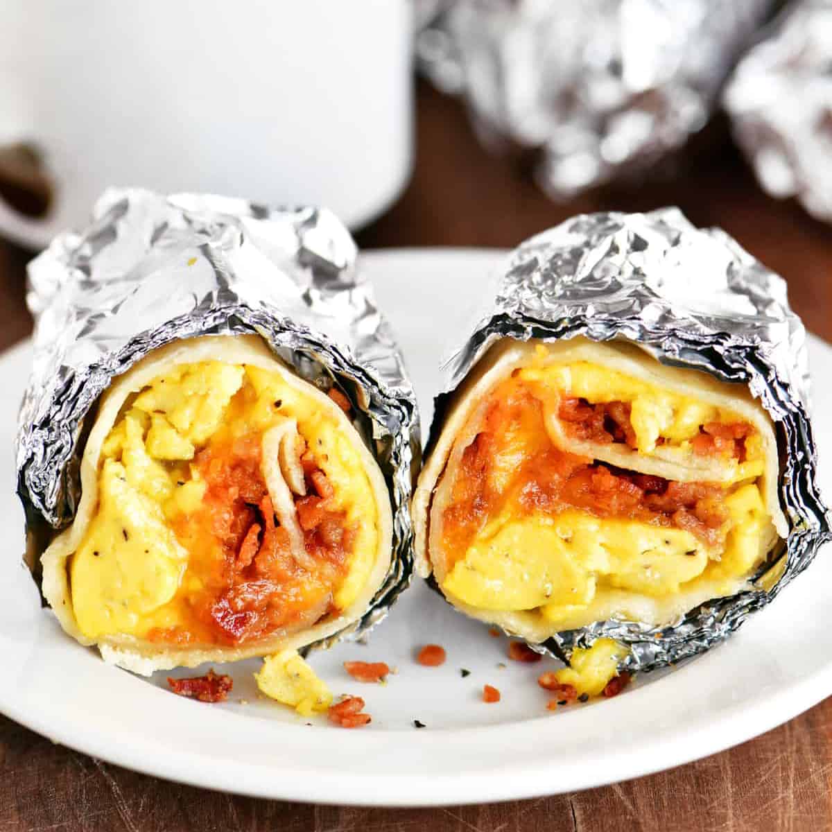 two foil wrapped breakfast burritios on a white plate.