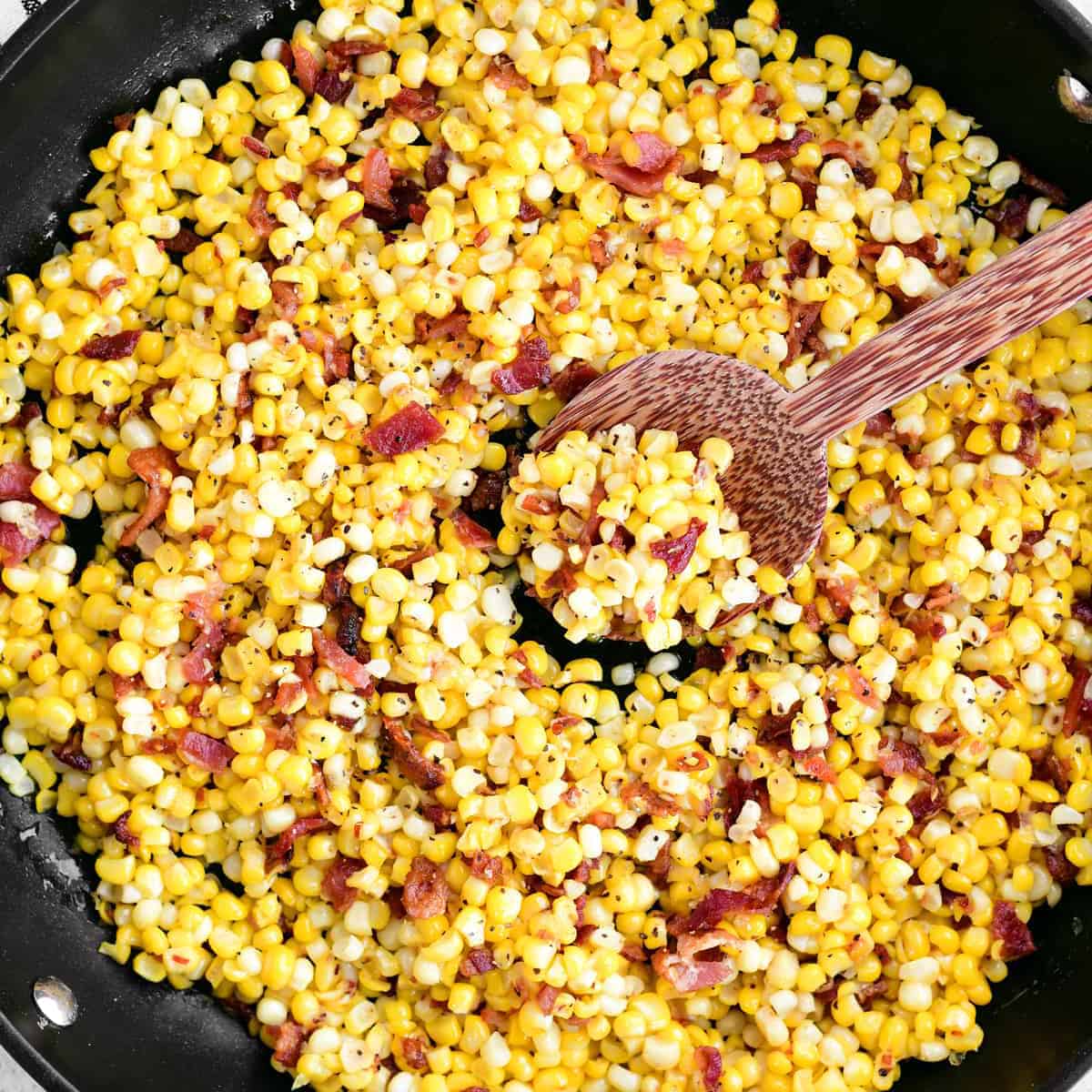 bacon fried corn in a skillet with a wooden spoon.