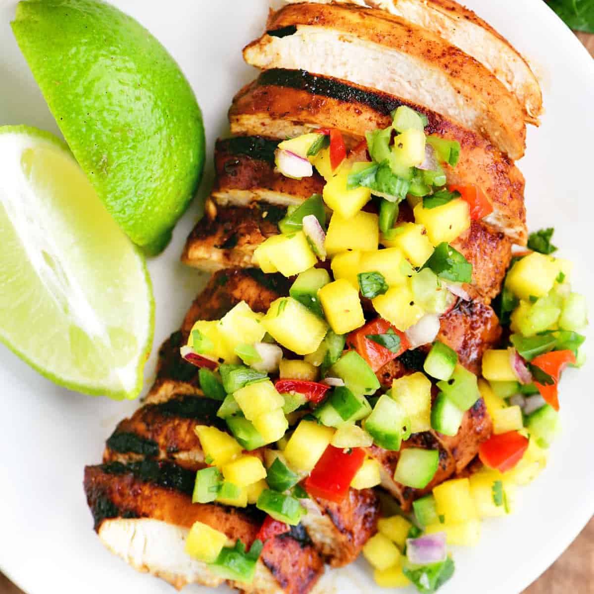 a sliced chicken breast topped with mango salsa on a white plate.