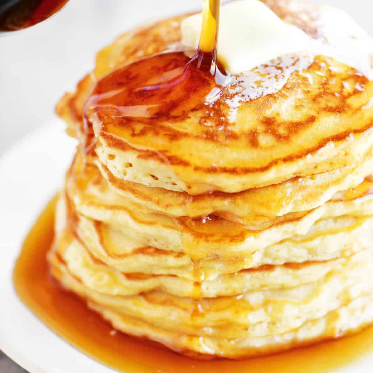 a stack of pancakes with syrup being poured onto them.