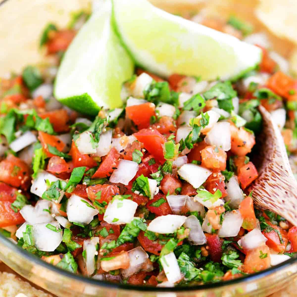 pico de gallo in a glass bowl with lime wedges on top.