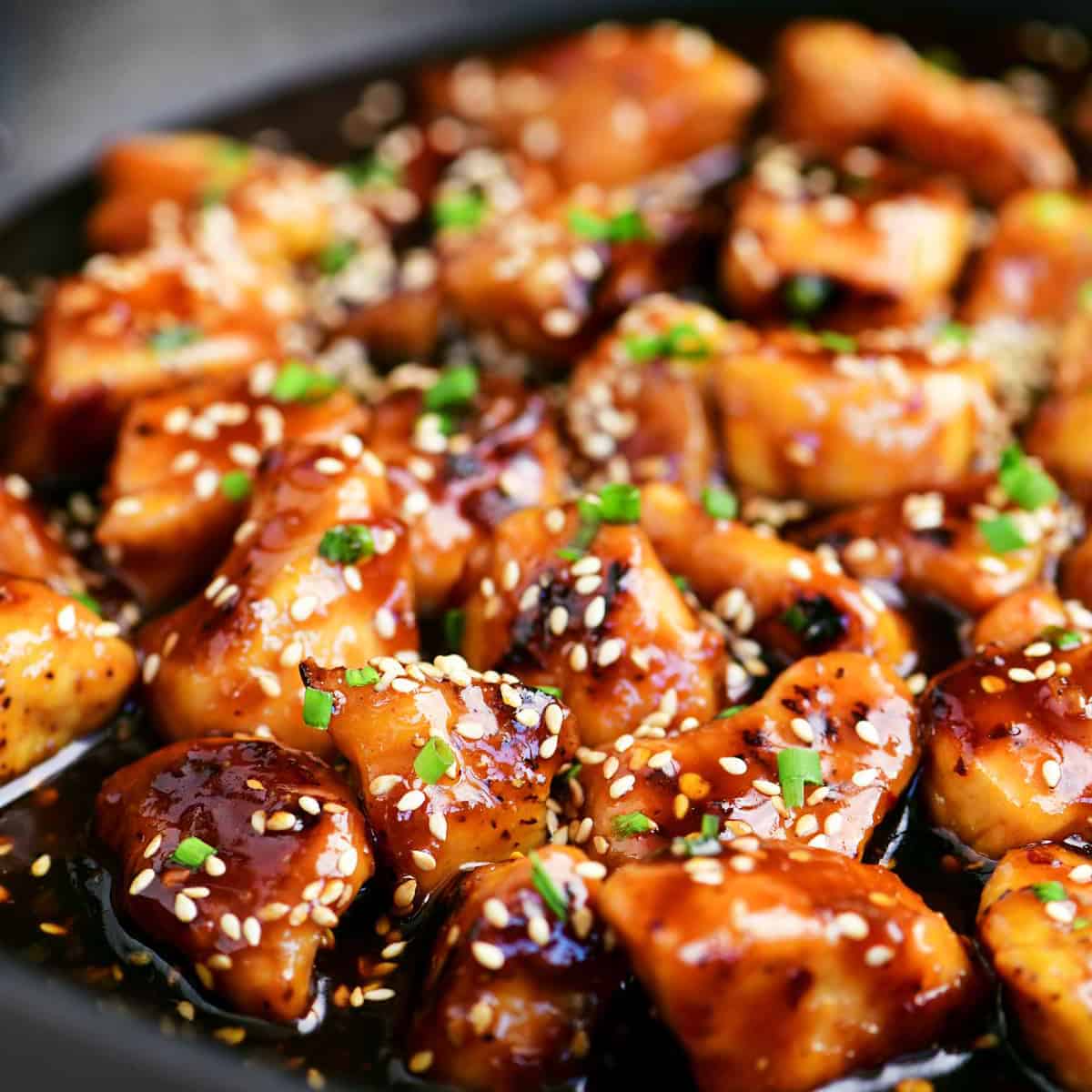 sesame chicken pieces in sauce topped with sliced green onions.