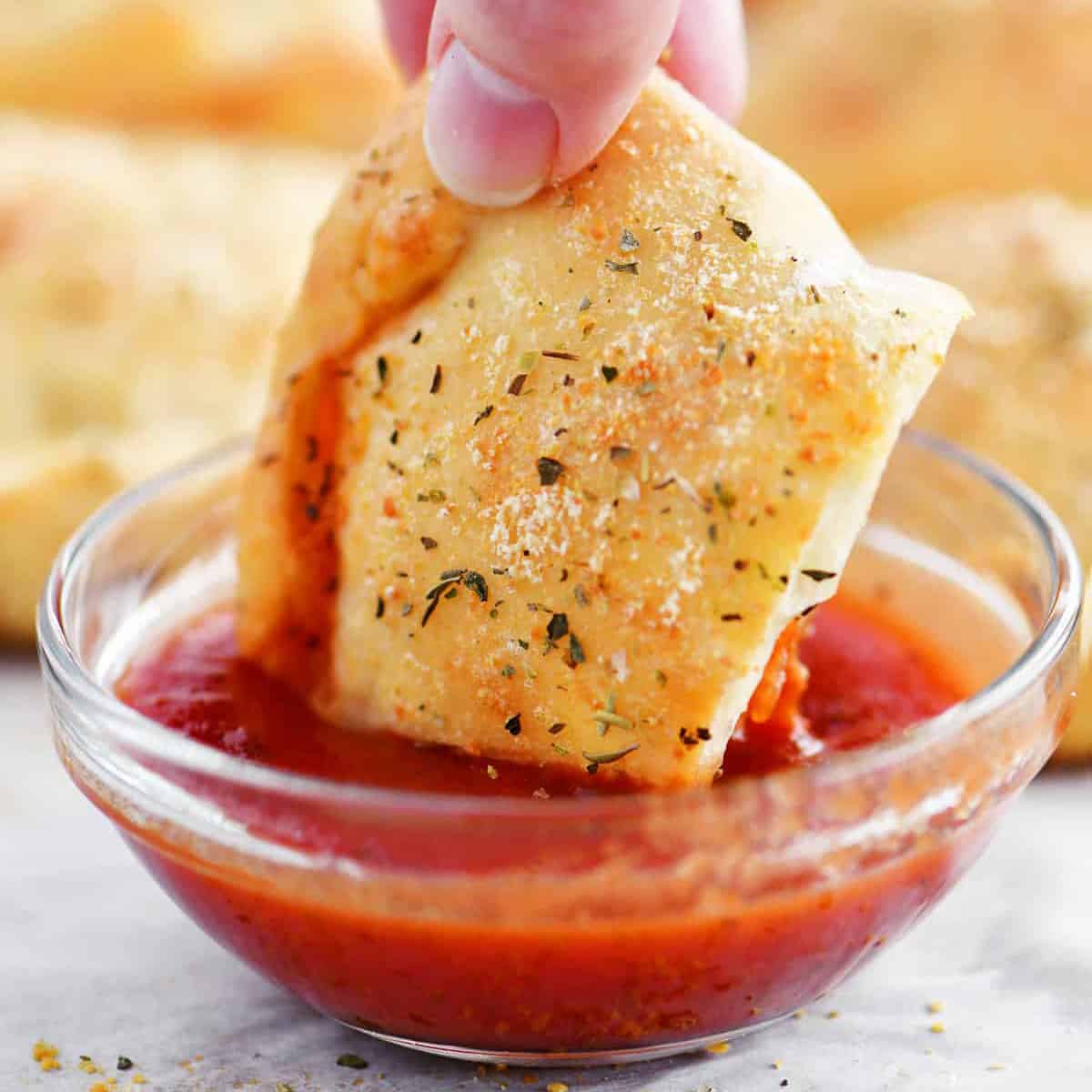 a hand dipping a calzone into pizza sauce.