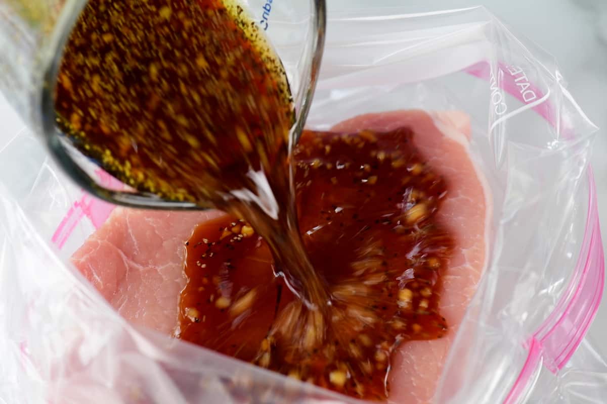 pouring marinade over pork chops in a gallon sized zip top bag.