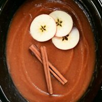 crock pot applesauce with sliced apples and cinnamon sticks.
