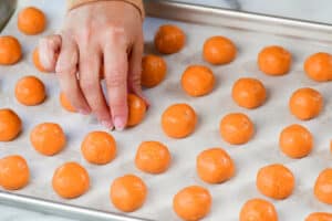 placing an orange oreo ball on a pan.