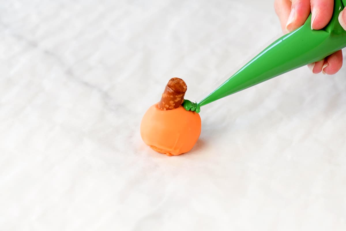 piping a green leaf on a pumpkin oreo ball.
