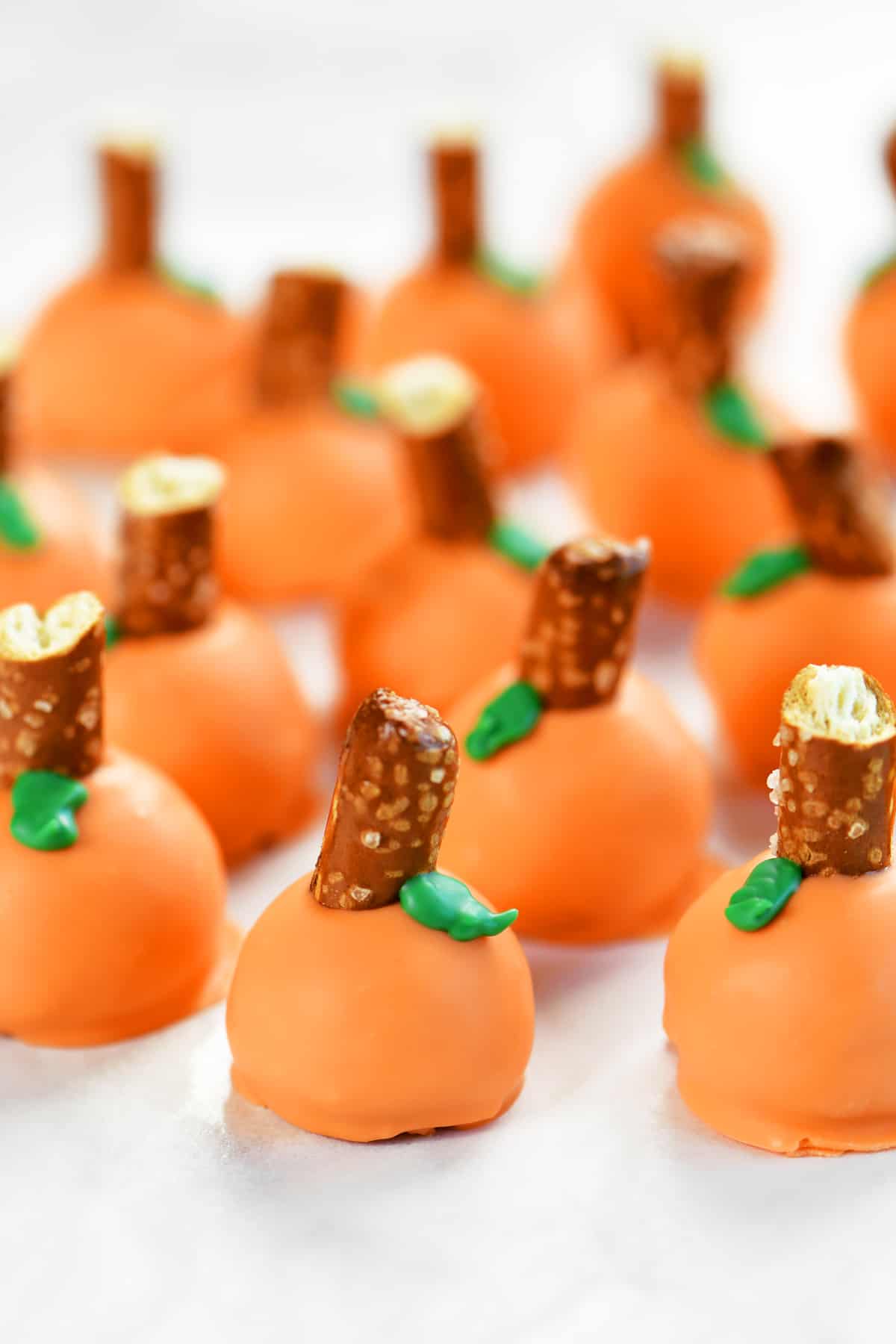 pumpkin oreo truffles with pretzel stems and green leaves.