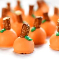 pumpkin oreo balls with pretzel stems and green leaves.