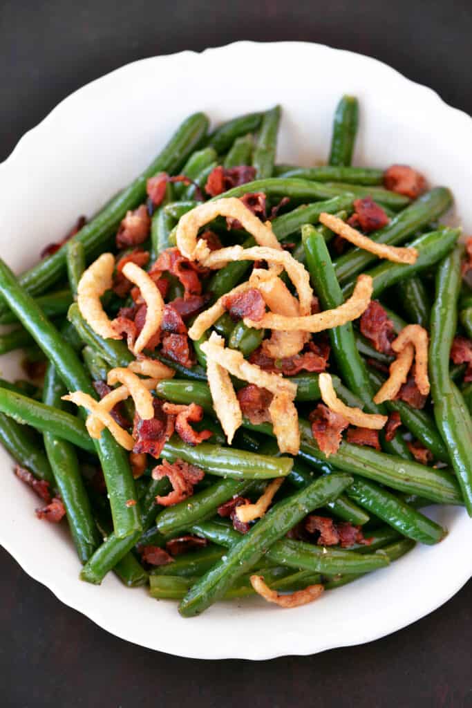 sauteed green beans topped with bacon and french fried onions in a white bowl