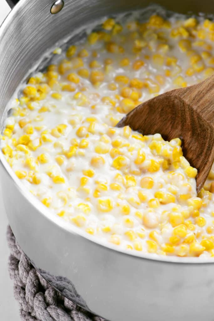 a wooden spoon and creamed corn in a pot.