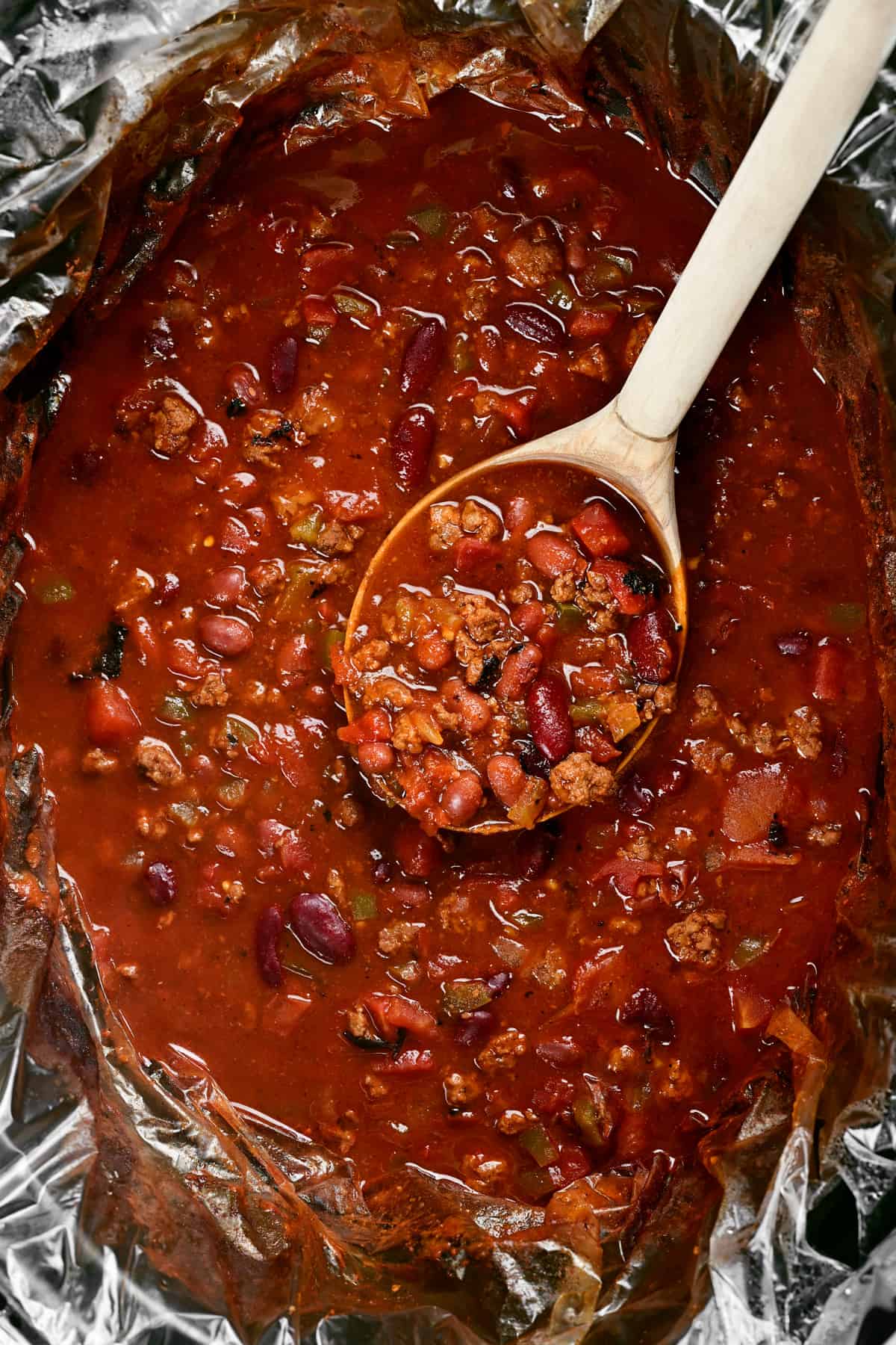a ladle full of chili in a crock pot.