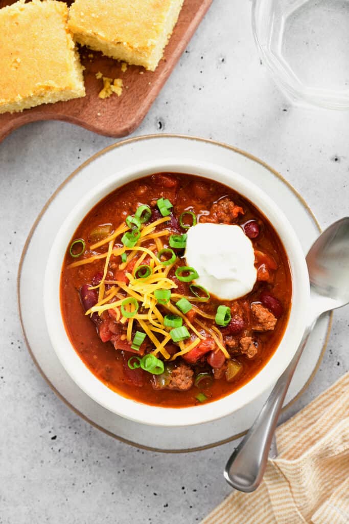 a bowl of chili, cornbread on a cutting board and a glass of water.