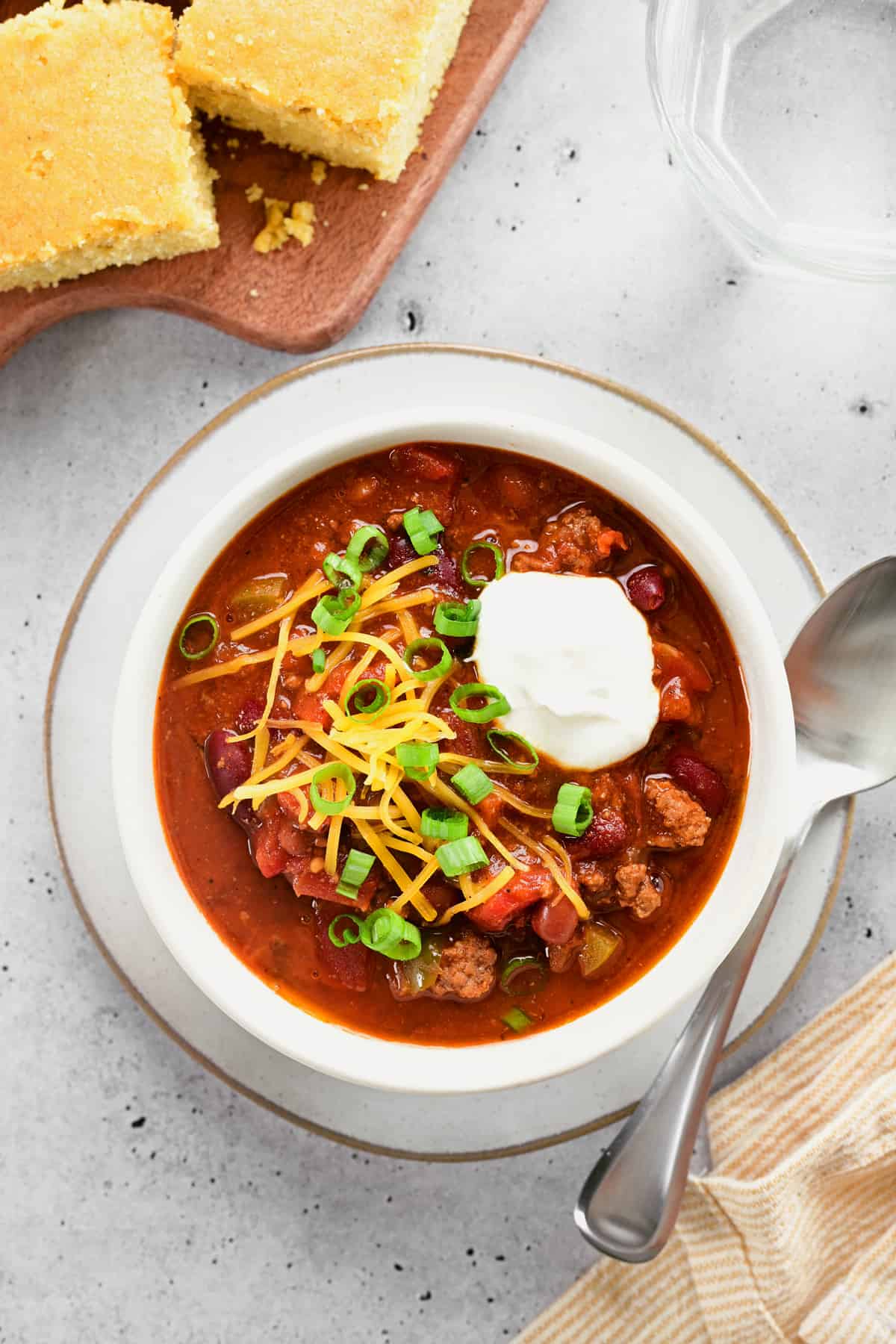 a bowl of chili, cornbread on a cutting board and a glass of water.