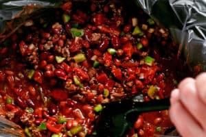 a hand stirs chili ingredients