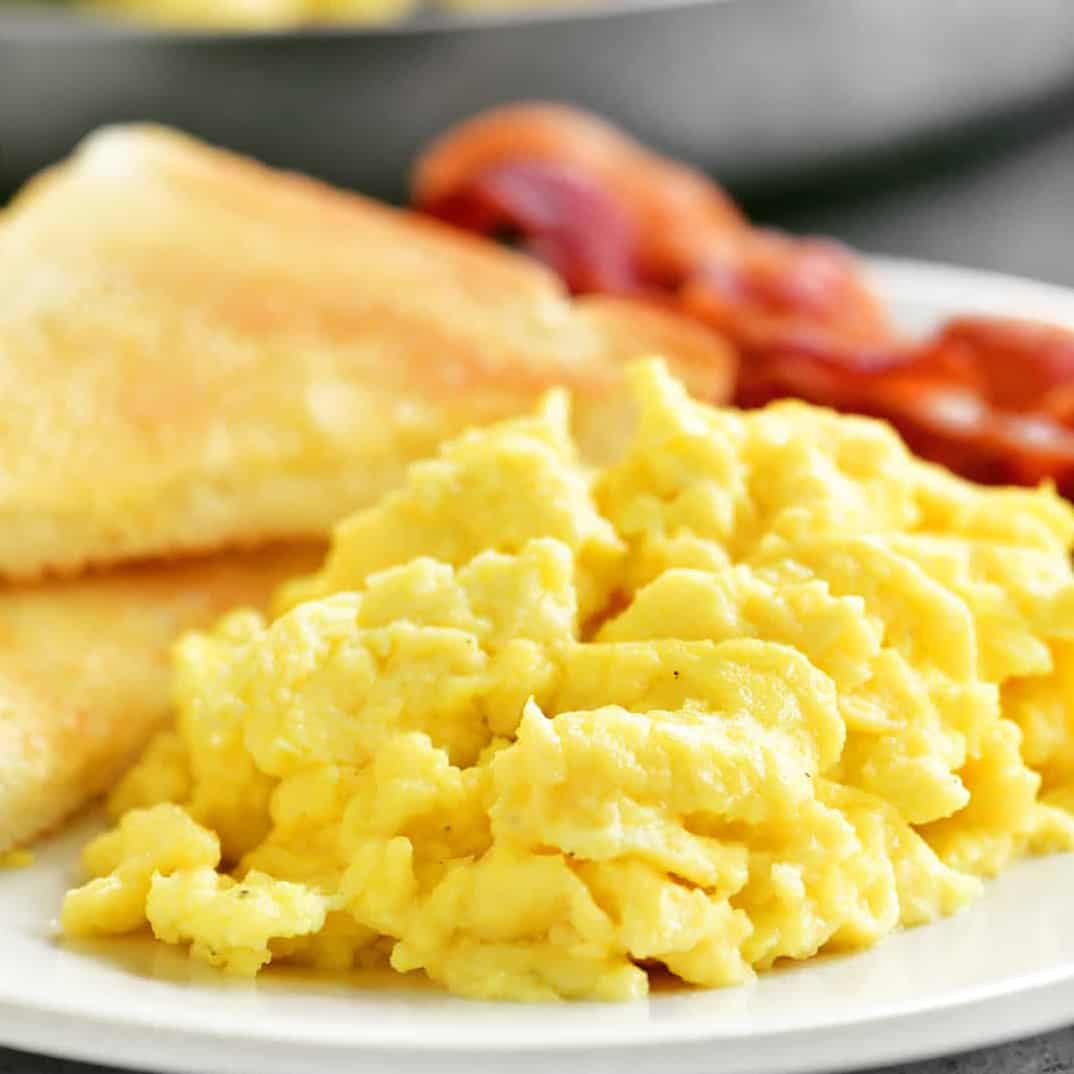 scrambled eggs on a plate with toast and bacon.