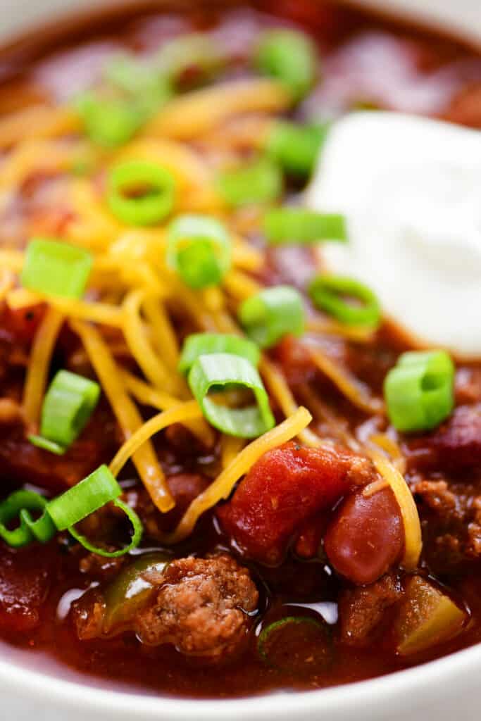close up view of chili in a white bowl topped with onions and sour cream.