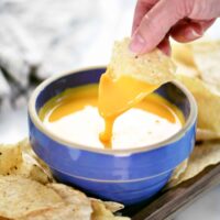 a hand dipping a chip into cheese.