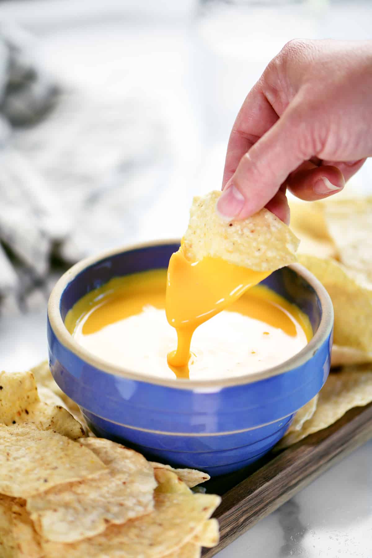 a hand using a chip to scoop up cheese dip from a blue bowl.
