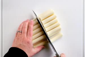 hands using a kitchen knife to cut cheese sticks.