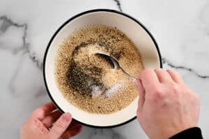 a hand using a spoon to stir breading ingredients.