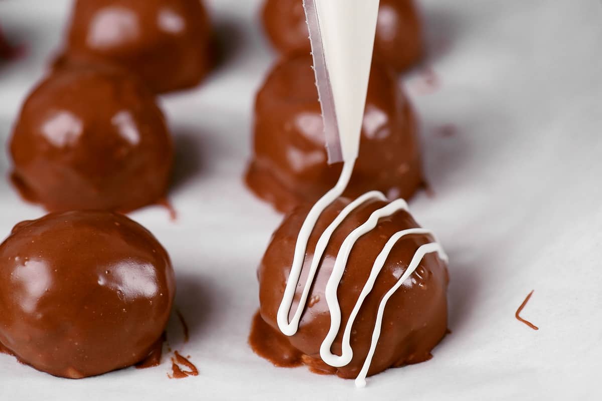 drizzling melted white chocolate over chocolate coated peanut butter balls.
