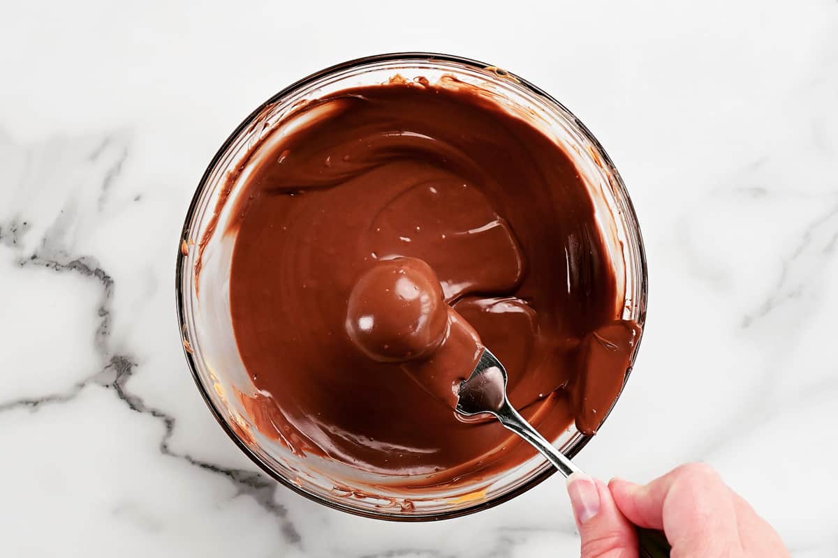 a hand holding a fork with a chocolate ball of a bowl of melted chocolate.