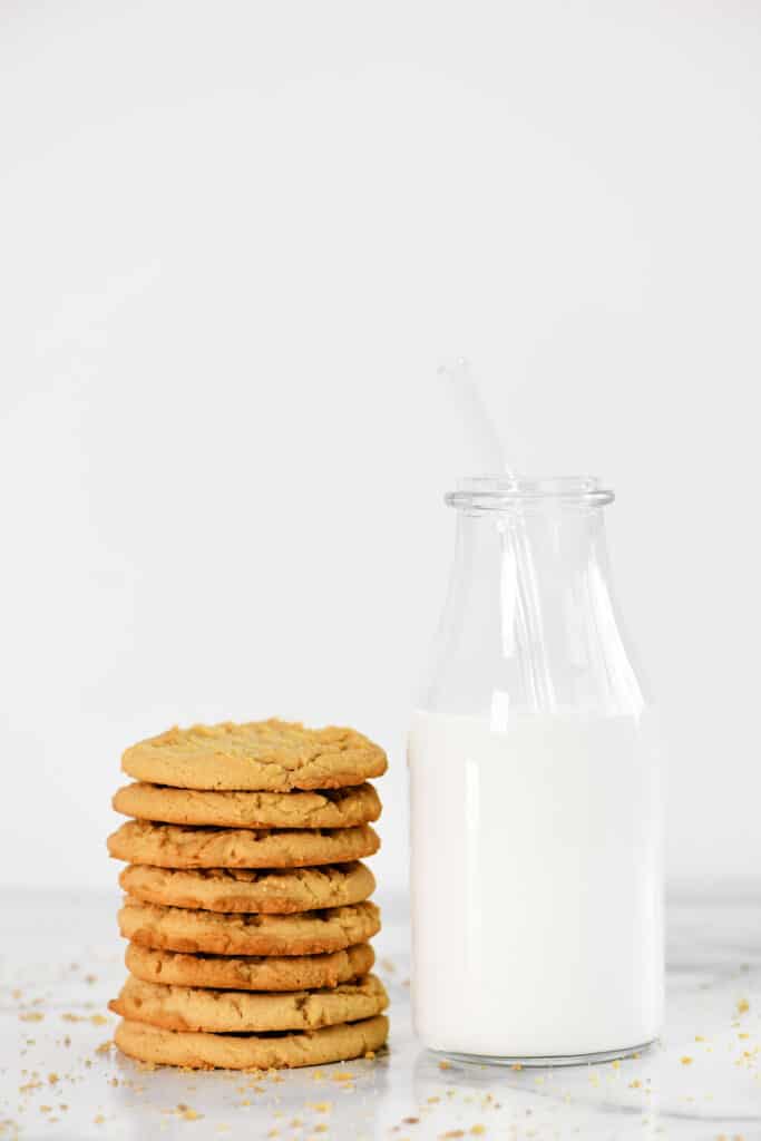 a stack of peanut butter cookies with a carafe of milk.