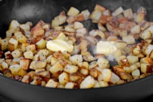 pats of butter on top of diced potatoes cooking in a pan.