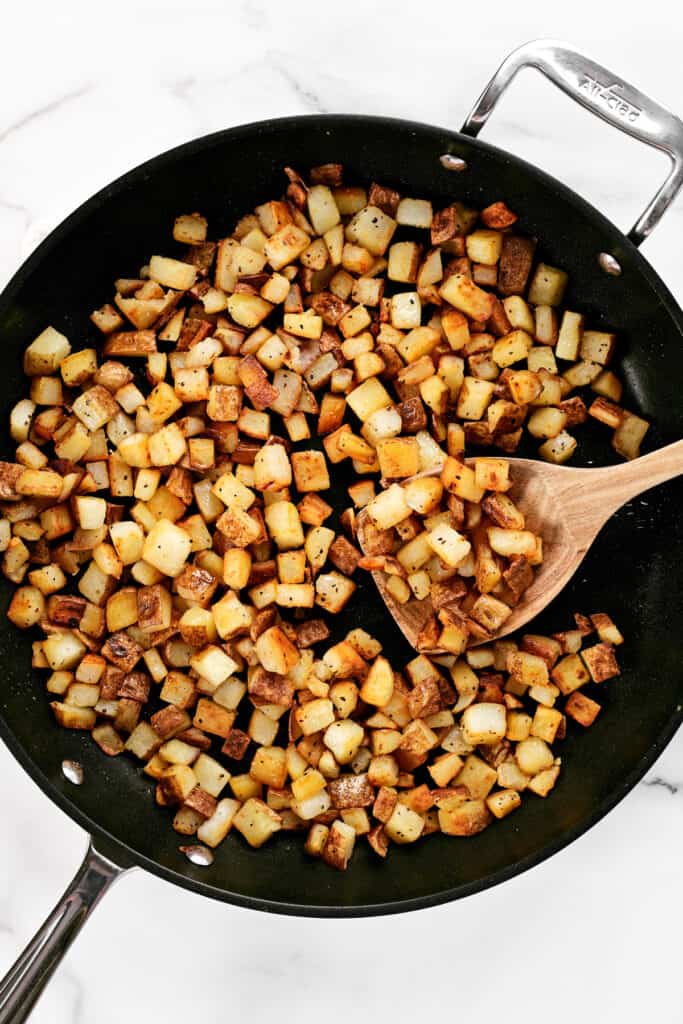 a wooden spoon in a frying pan with breakfast potatoes.
