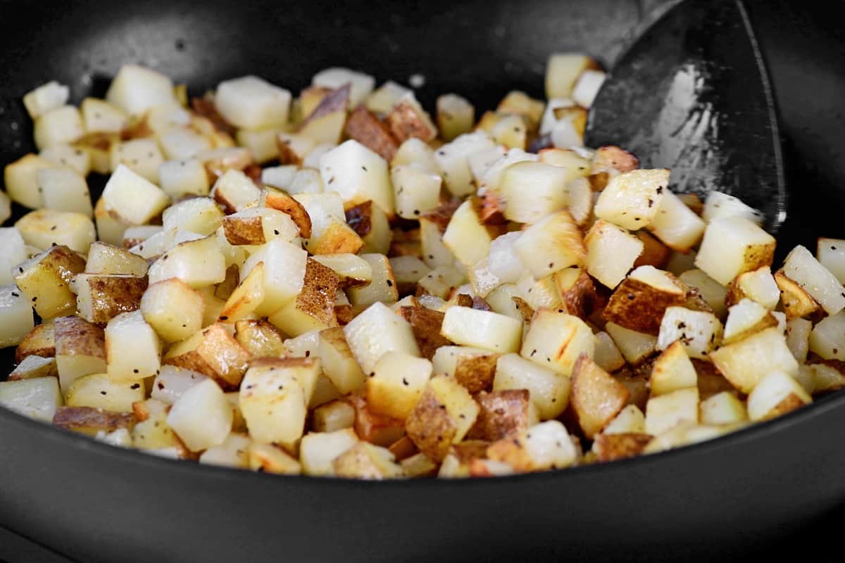 a rubber spoon stirs potatoes in a pan while they cook.